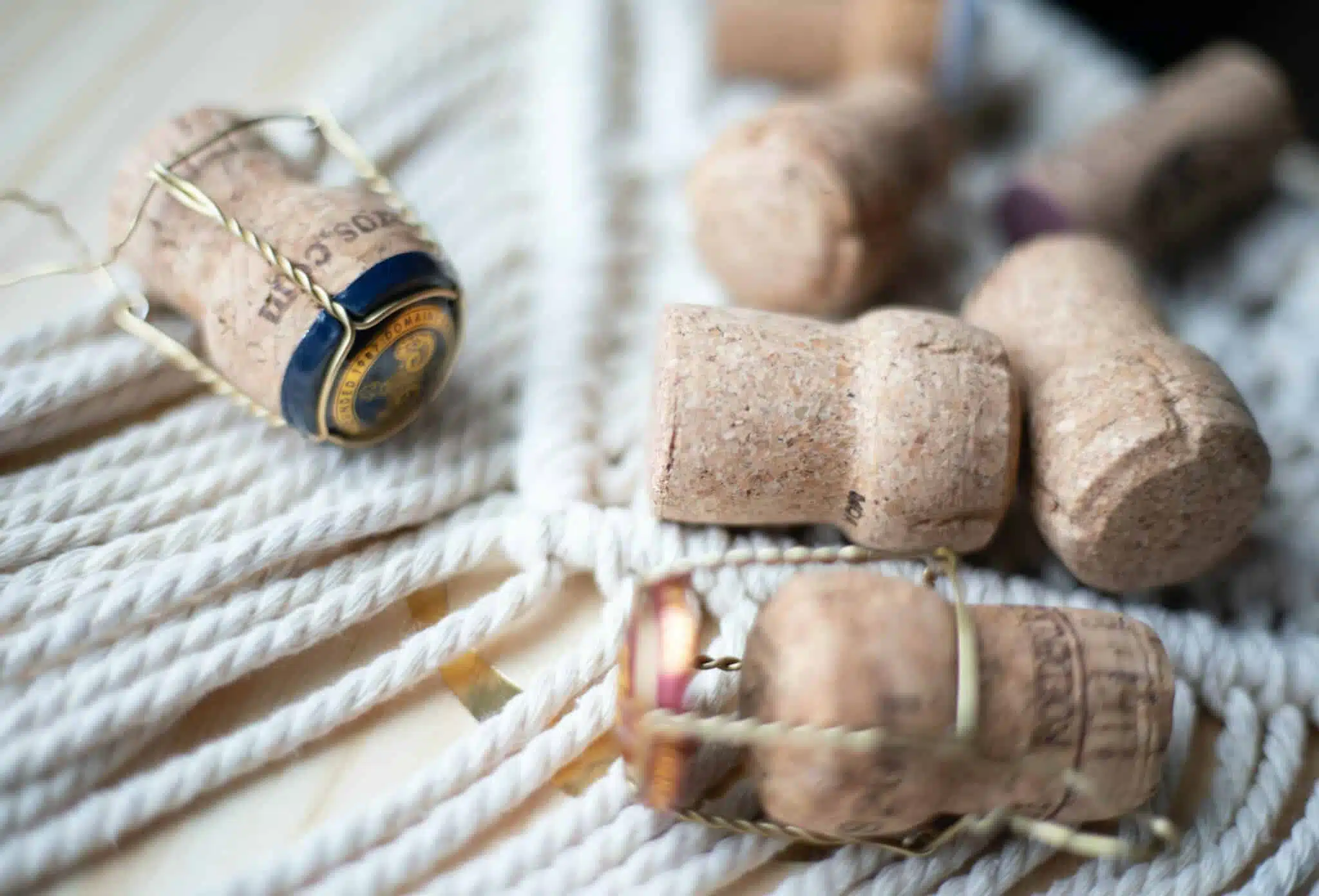 Several champagne corks and wire cages scattered on a light rope surface, with one cork cap visible and a foil seal.